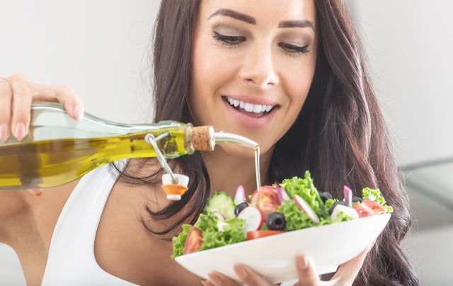 young attractive woman pours olive oil into a healthy vegetable salad